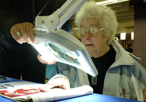 Une personne âgée teste une loupe avec éclairage lors du BrailleTech 2015.