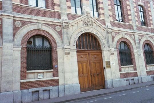 Photo de l'entrée sous arc cintré abritant deux portes en bois et flanquée de baies grillagées