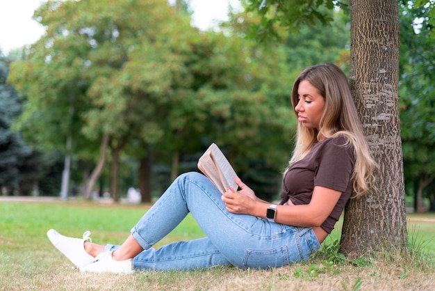 Portrait D'une Belle Lectrice De Jolie Fille, Jeune Femme, étudiante Lit Un  Livre Intéressant Dans Un Parc D'été, Assise Sur Le Sol, Herbe Verte,  S'appuyant Sur Un Arbre. | Photo Premium