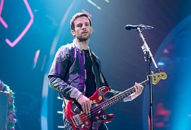 A short-haired man wearing a dark-coloured jacket plays the bass