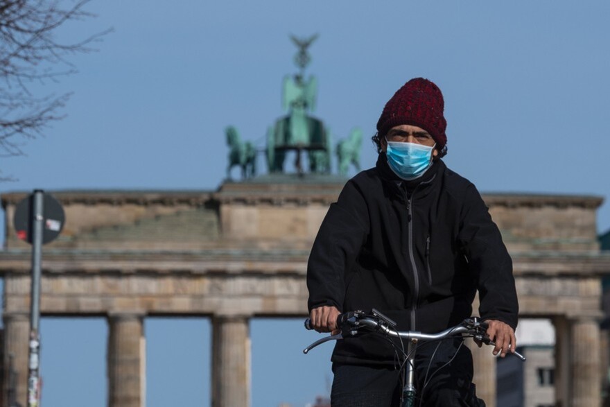 Un homme portant un masque fait du vélo devant la porte de Brandebourg, à Berlin, en Allemagne