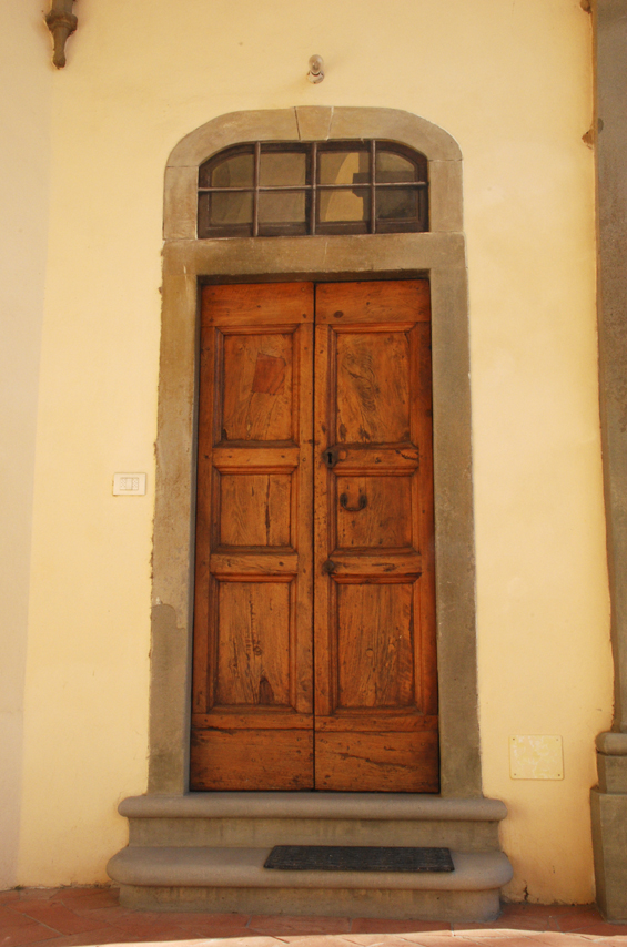 Photo en couleurs d'une porte en bois assez simple, dans un mur blanc.