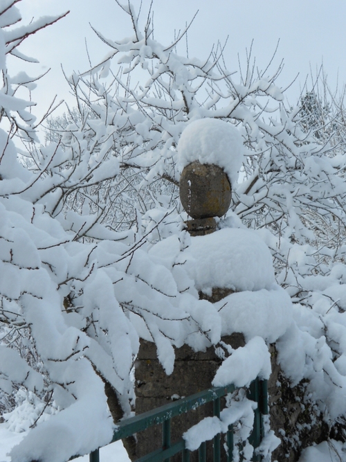au  milieu de branches enneigées, un pilier de portail, surmonté d'une pierre ovoïde, l'épaisse couche de neige donne l'illusion d un chapeau et d'une écharpe