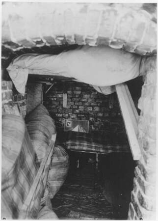 Photo prise depuis l'entrée étroite d'une cave. Au fond, une couchette recouverte d'une couverture à carreaux.