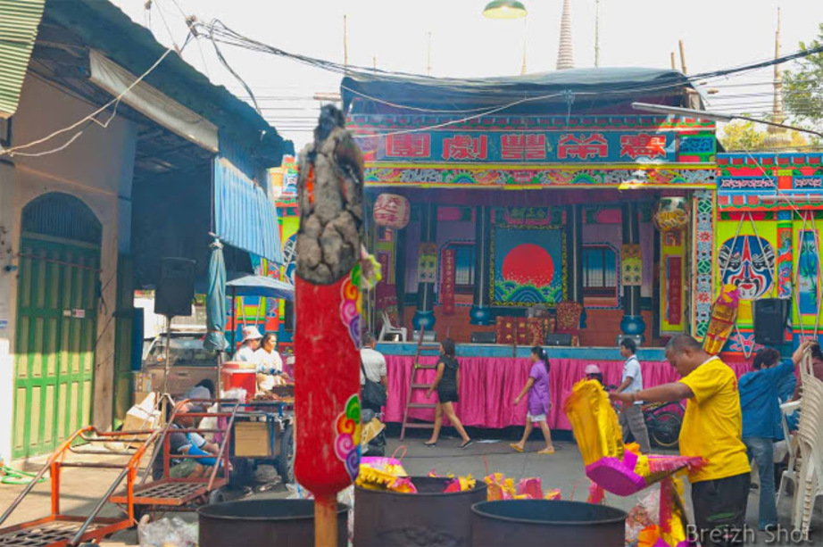 Une fête chinoise près du Chao Phraya à Bangkok :  Un grand cierge incandescent se consume tandis que des décorations festives sont mises dans des containers pour être brûlés.