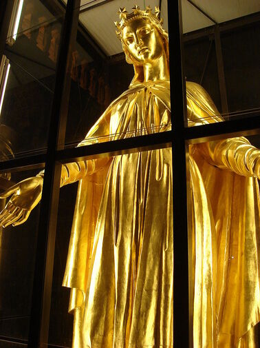 Photographie couleur de la statue de Marie, de près et en contre-plongée, sous une cage de verre.