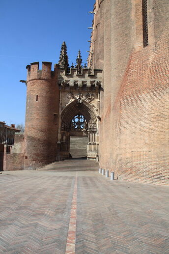 photo couleur d'une porte fortifiée établie entre une tour et la cathédrale en briques. La porte elle-même est en pierre, très sculptée, à portail ressemblant à celui d'une église.