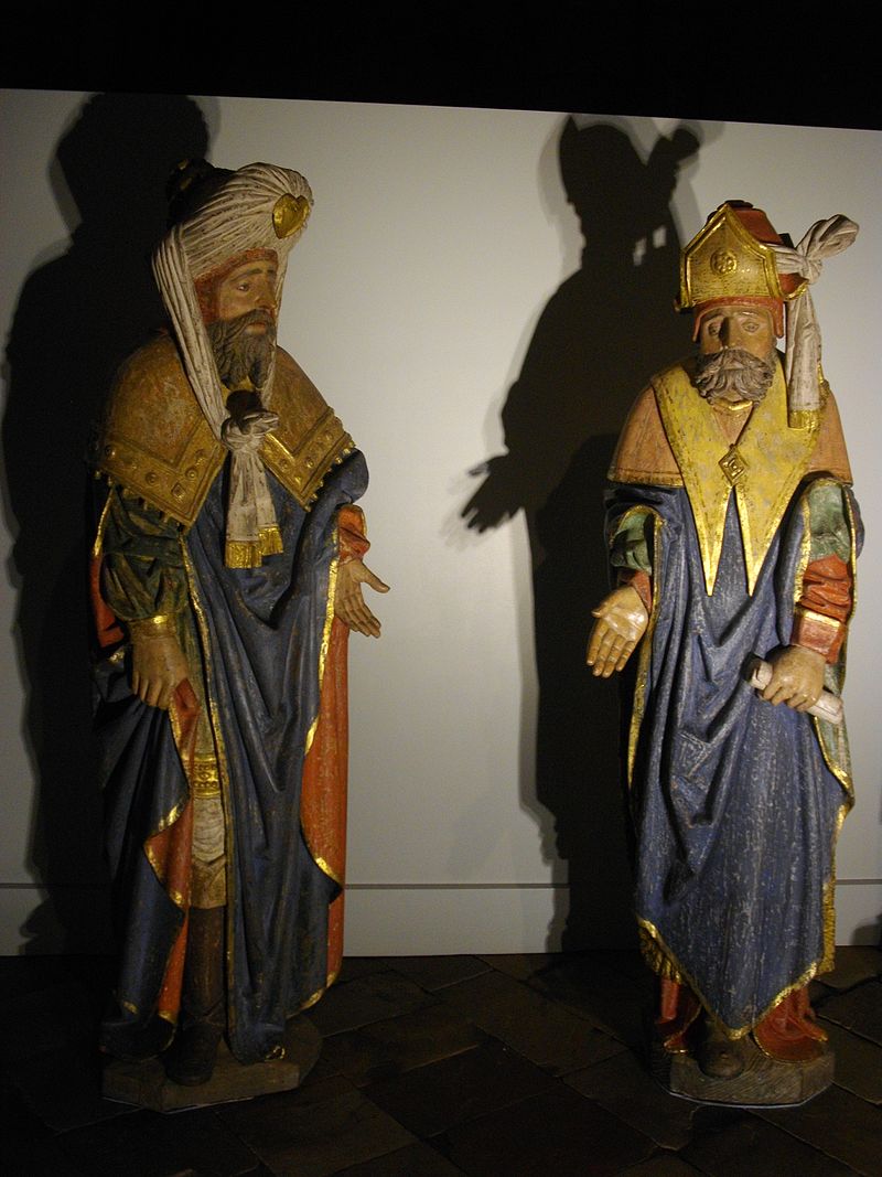 Photo couleur de deux personnages en bois sculpté et coloré sur fond blanc.