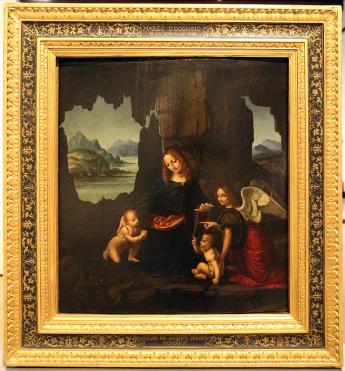 Tableau en couleur. Dans un cadre de rochers, une femme est entourée de deux bébés nus. L'un est agenouillé l'autre est assis. Un personnage habillé et ailé regarde l'observateur et désigne le bébé de gauche du doigt.